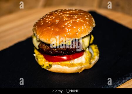 Dettaglio di cheeseburger di manzo fresco e gustoso con formaggio fuso isolato su sfondo nero Foto Stock