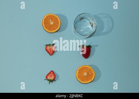 Un primo piano di frutta estiva disposizione con frutta fresca e un bicchiere d'acqua su sfondo blu Foto Stock