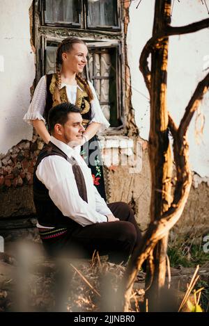 Un primo piano di una giovane coppia serba in costume tradizionale di fronte alla casa rurale Foto Stock