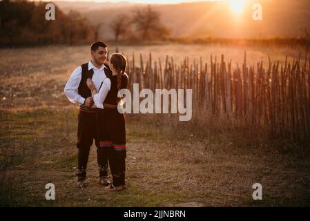 Un primo piano di una giovane coppia serba in costume tradizionale sul campo Foto Stock