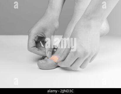 Donna che applica cerotto medico sulle dita dei piedi. Primo soccorso, concetto di medicina. Tagli, abrasioni e ferite leggermente sanguinanti, cicatrizzazione dei corni. Bianco e nero. Foto di alta qualità Foto Stock