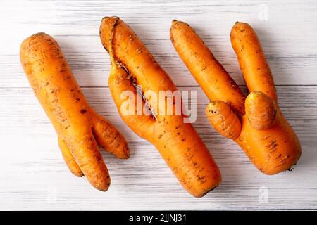 Su una superficie di legno chiaro giacciono diverse carote brutte di arancio mature Foto Stock