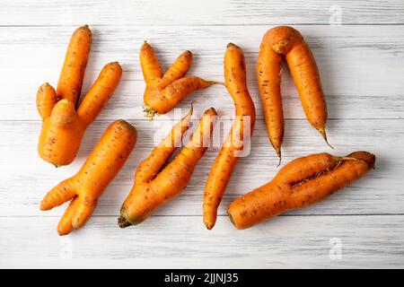 Su una superficie di legno chiaro giacciono diverse carote brutte di arancio mature. Foto Stock