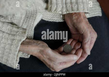 Le mani di una donna tengono una moneta di 50 lari georgiani. Pensione, povertà, problemi sociali e il tema della vecchiaia. Conservazione. Foto Stock