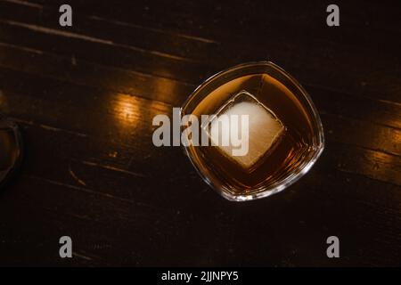 Una vista dall'alto di un bicchiere di whiskey con un cubetto di ghiaccio su un tavolo di legno Foto Stock