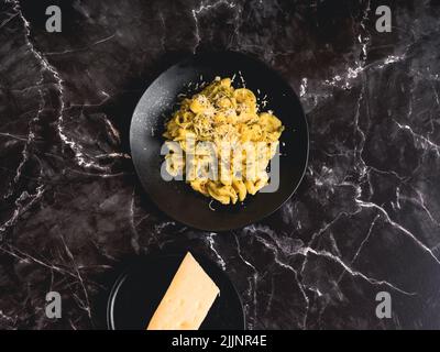 Un colpo di tortellini con parmigiano sulla superficie di marmo nero Foto Stock