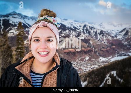 Una donna caucasica felice con capelli biondi in piedi sullo sfondo delle montagne coperte di neve del Colorado Foto Stock