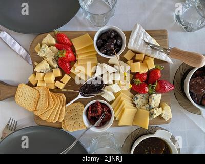 Piatto di formaggi con camembert, brie, dor blue, fragole, pomodori secchi, olive su un tavolo di legno, vista dall'alto. Foto Stock
