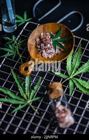 Vista dall'alto delle foglie di marijuana e del sale Himalayano rosa in vasetti di vetro su una roccia di raffreddamento in metallo Foto Stock