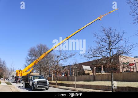 Gigantesca gru gialla allestita su strade urbane bloccate che si estendono sopra l'edificio abbassando qualcosa in esso Foto Stock