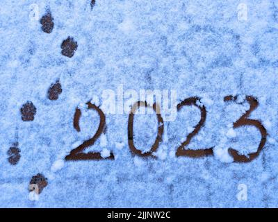 Testo felice anno nuovo 2023 sulla neve. Iscrizione manoscritta 2023 e tracce del prossimo anno su neve bianca appena caduta. Fo di sfondo astratto Foto Stock