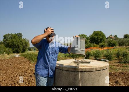 Immagine di un contadino disperato con un secchio vuoto perché non c'è più acqua nel pozzo. Riferimento al cambiamento climatico e alla siccità in agricoltura Foto Stock