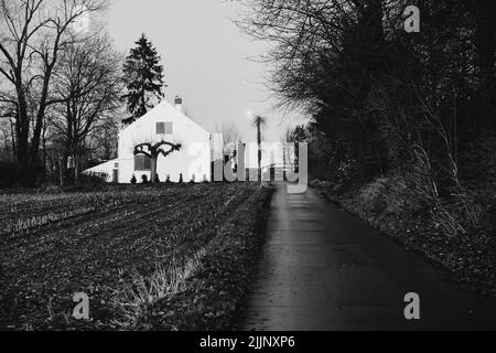 Una foto in scala di grigi di un percorso che conduce ad una vecchia chiesa di Maransart, Belgio Foto Stock