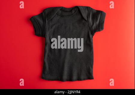 Mockup piatto di una t-shirt nera in cotone per bambini su sfondo rosso. Sport vestiti comodi per le ragazze. Layout per l'applicazione di stampe, logo. Chi Foto Stock