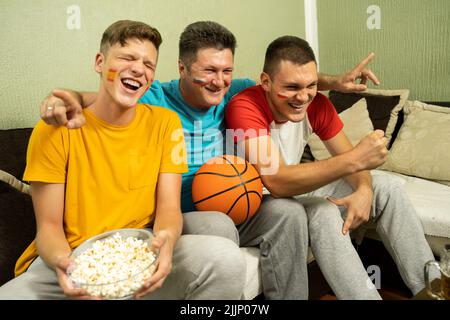 Tre fan maschili di basket che guardano il gioco e celebrano la vittoria Foto Stock