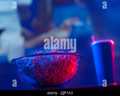 Sullo sfondo dello schermo di una grande TV al plasma, una ciotola di vetro di popcorn e una bevanda di soda in un vetro di plastica. Riposati a casa, guardando la TV con Foto Stock