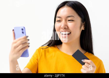 Shopping online, concetto di tecnologia felice donna asiatica tenendo cellulare e carta di credito su sfondo bianco Foto Stock