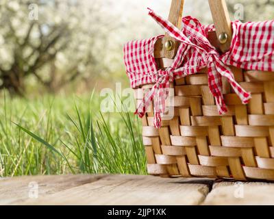 Su un tavolo di legno si trova un cestino da picnic di paglia splendidamente decorato sullo sfondo della natura estiva. Attività ricreative all'aperto, picnic. Vacanze, vacanze Foto Stock