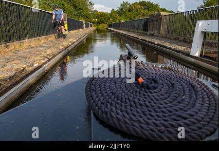 Scozia, Regno Unito, 27th luglio 2022. UK Weather: Serata di sole sul canale Union. Un ciclista in bicicletta sulla via del canale mentre una barca stretta attraversa l'acquedotto delle mandorle nel Lothian occidentale Foto Stock