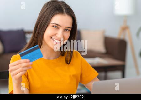 Giovane donna tenere carta di credito bancario, shopping online utilizzando il laptop, acquistare beni o ordinare online Foto Stock