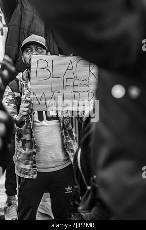 Un colpo verticale in scala di grigi di un uomo che ha un segno di 'BLACK LIFES MATTERa' durante la protesta a Glasgow, Regno Unito Foto Stock