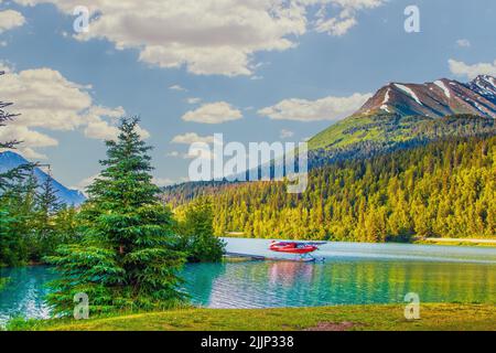 Idrovolante rosso sul lago a Moose Pass, Alaska in sole serale con montagne sullo sfondo e circondato da alberi sempreverdi Foto Stock