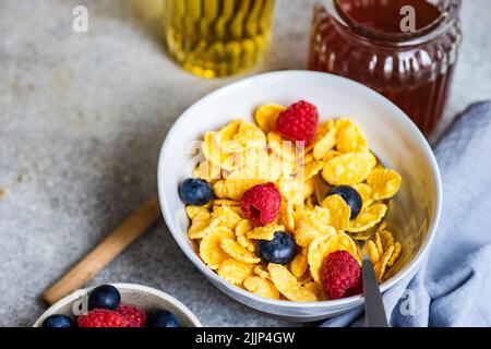 Primo piano di una ciotola di fiocchi di mais con lamponi freschi, mirtilli, miele e un bicchiere di succo Foto Stock