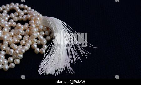 Su uno sfondo blu scuro si trova una collana di perle e una nappina di seta bianca. Gioielli per la sposa per il matrimonio. Foto Stock