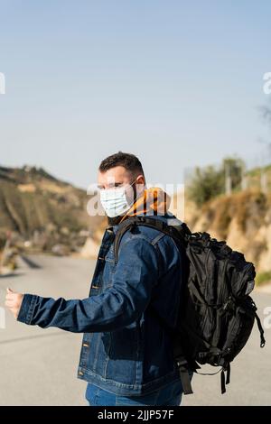 Un colpo di uomo caucasico che indossa la maschera e fa hitchhiking Foto Stock