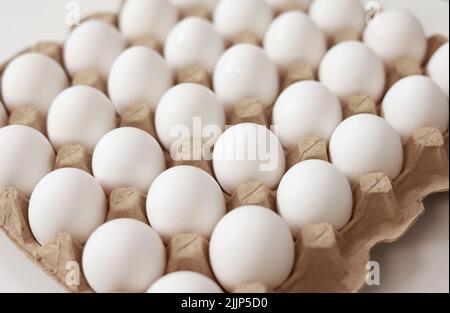 Primo piano delle uova di pollo crude in vassoio di carta per uova su sfondo bianco. Gruppo di uova bianche fresche in una cassetta di cartone. Cibo biologico dalla natura buono per la salute Foto Stock