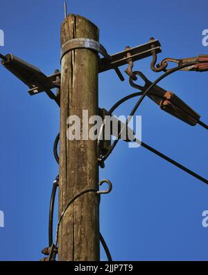 Un basso angolo verticale primo piano di un palo di legno di elettricità contro il cielo blu chiaro sfondo Foto Stock