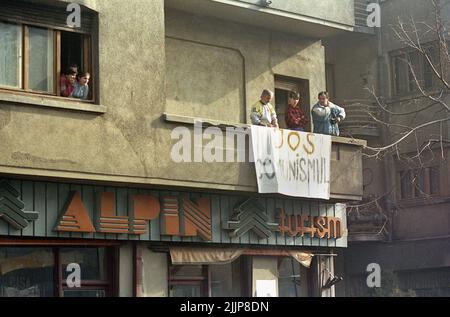 Bucarest, Romania, gennaio 1990. La gente guarda i manifestanti nel centro di Bucarest dal loro appartamento, mostrando una bandiera che dice 'Down with Communism'. Dopo la rivoluzione anti-comunista del dicembre 1989, i disordini civili continuarono, poiché la maggior parte delle nuove persone al potere erano gli ex ufficiali comunisti. Foto Stock