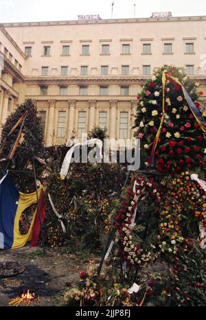 Bucarest, Romania, gennaio 1990. Fiori a Piata Palatului/ Piata Revolutiei per le vittime della rivoluzione anticomunista del dicembre 1989. In cima all'edificio governativo, si può leggere "Long Live Romania”, dopo la rimozione delle parole intermedie 'la repubblica socialista di '. Foto Stock