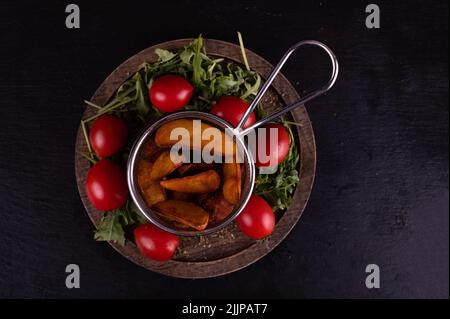 Vista dall'alto di un cestino con spicchi di patate, pomodori ciliegini e razzo Foto Stock