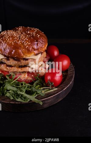 Primo piano di un doppio hamburger di formaggio di pollo con pomodori ciliegini e razzo Foto Stock