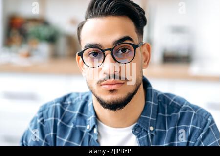 Primo piano ritratto di un bel giovane indiano o arabo moderno con occhiali, con una barba, vestito elegantemente, studente, freelancer, Specialista IT, che guarda direttamente la fotocamera Foto Stock