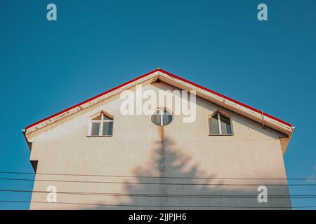 Un'immagine ad angolo basso di un edificio con un'ombra di albero sulla sua facciata bianca isolata su uno sfondo blu cielo Foto Stock