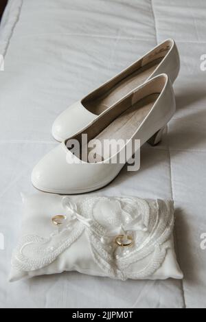 closeup verticale di scarpe da matrimonio bianche e anelli d'oro in attesa del loro proprietario Foto Stock