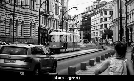 Una foto in scala di grigi di persone che camminano in una strada trafficata con diversi edifici a Praga, Repubblica Ceca Foto Stock