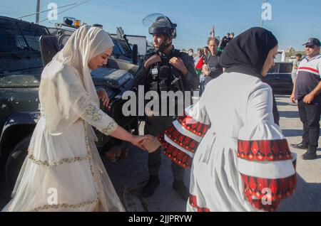 Haris Village, Palestina. 27th luglio 2022. Una sposa palestinese e la sua amica passano davanti ad un soldato israeliano in un checkpoint israeliano dopo che la processione delle nozze è stata impedita all'ingresso del villaggio di Haris nella Cisgiordania occupata. Credit: SOPA Images Limited/Alamy Live News Foto Stock