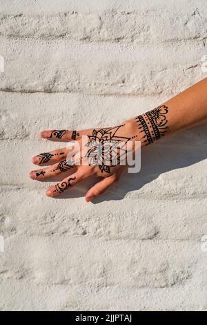 Mano di una donna con henné che si disegna su una parete di mattoni di colore bianco Foto Stock