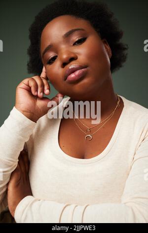 Ive mi ha dato qualcosa in mente: Una giovane donna attraente che guarda contemplativa mentre si posa su uno sfondo verde nello studio. Foto Stock