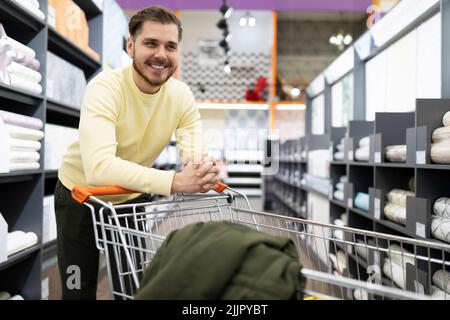 un cliente soddisfatto in un negozio di materiali decorativi e carta da parati si appoggia su un cestino di alimentari in metallo Foto Stock