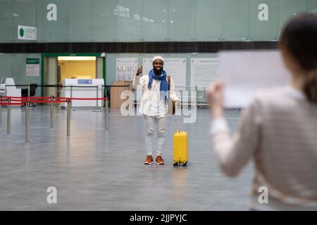 Giovane felice eccitato africano americano uomo viaggiatore in aeroporto ondeggiante con mano ad amico Foto Stock