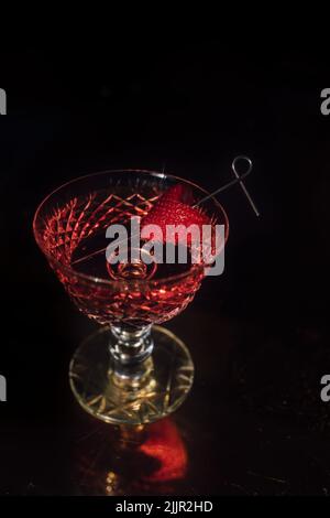 Un colpo verticale di un cocktail alcolico in un bel bicchiere con una fragola sulla paglia Foto Stock