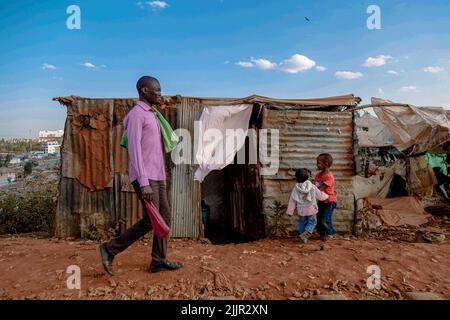 Un uomo cammina accanto ai bambini che giocano per strada nella Kibera Slum di Nairobi, Kenya. Vita all'interno della più grande Slum dell'Africa di Kibera. Foto Stock