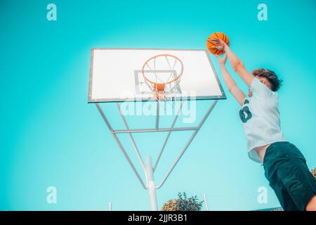 Un angolo basso di un giovane maschio che inzuppa una pallacanestro nel cerchio Foto Stock