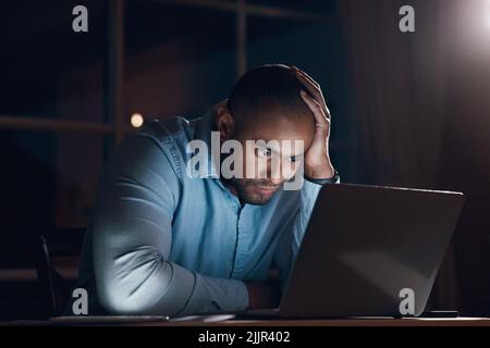 Che cosa sto andando fare: Un giovane uomo d'affari che guarda stressato mentre lavora sul suo portatile a tarda notte. Foto Stock