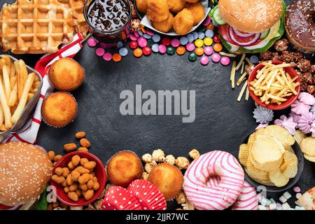 Prodotti malsani. Cibo cattivo per figura, pelle, cuore e denti. Assortimento di alimenti a base di carboidrati veloci con patatine fritte e cola su sfondo scuro. Top vi Foto Stock