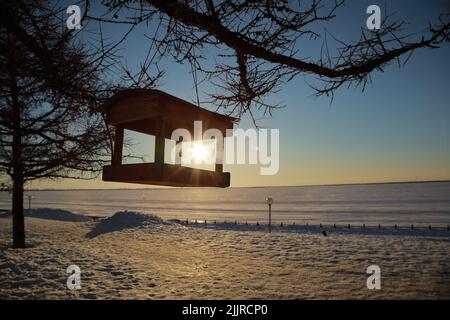 Un gazebo sospeso in legno in un campo nevoso durante il tramonto Foto Stock